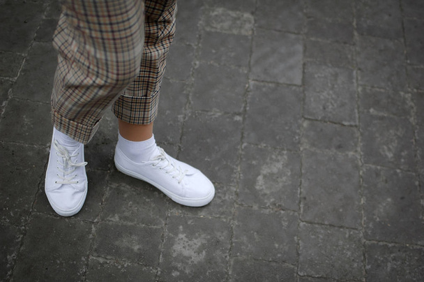 Zijaanzicht van jonge Womens voet in witte sneakers op asfalt achtergrond. - Foto, afbeelding