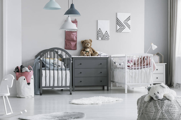 Brown teddy bear on grey wooden commode between two cribs in fashionable bedroom for twins - Foto, afbeelding