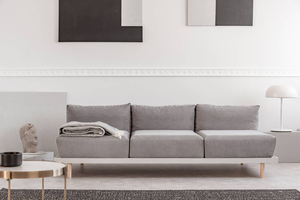 Сірий диван в білому інтер'єрі з абстрактними картинами на стіні
 - Фото, зображення