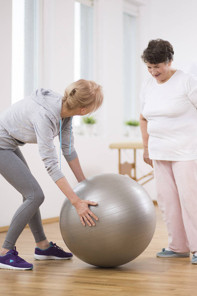 Senior woman and middle age physiotherapist with gymnastic ball - Photo, Image