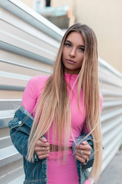 Glamour houkutteleva nuori nainen blondi pitkät hiukset vintage vaaleanpunainen shortsit tyylikäs vaaleanpunainen toppi trendikäs denim takki seisoo kadulla lähellä metalli hopea seinä kesäpäivänä. Söpö tyttö.
. - Valokuva, kuva