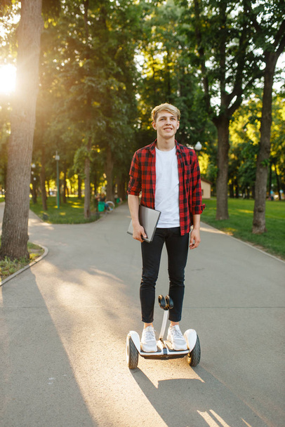 Młody człowiek jeżdżący na mini żyroskopie w letnim parku. Rekreacja na świeżym powietrzu z elektryczną żyrodeską. Ekologiczny transport z technologią wyważenia, elektryczny pojazd żyroskopowy - Zdjęcie, obraz