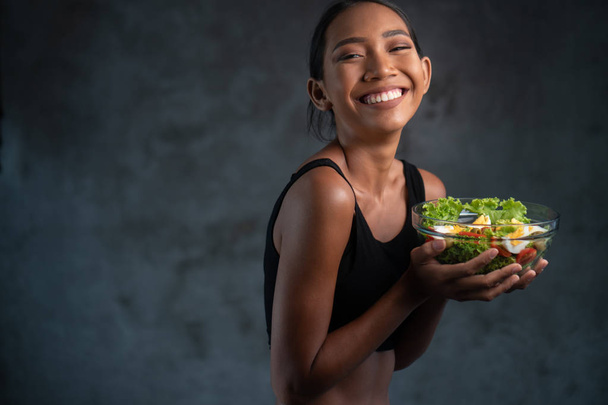 Portré szép fiatal mosolygós nő, fekete póló gazdaság tálba egészséges salátát konkrét háttér - Fotó, kép