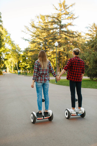 junges Paar reitet auf Gyroboard im Park, Rückansicht. Outdoor-Erholung mit elektrischem Gyroboard. Transport mit Balance-Technologie - Foto, Bild