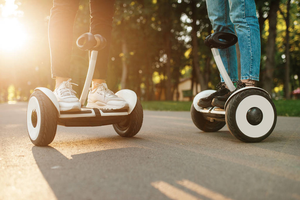 Male and female person riding on gyro board in park at sunset. Outdoor recreation with electric gyroboard. Transport with balance technology, gyroscope - Foto, Bild