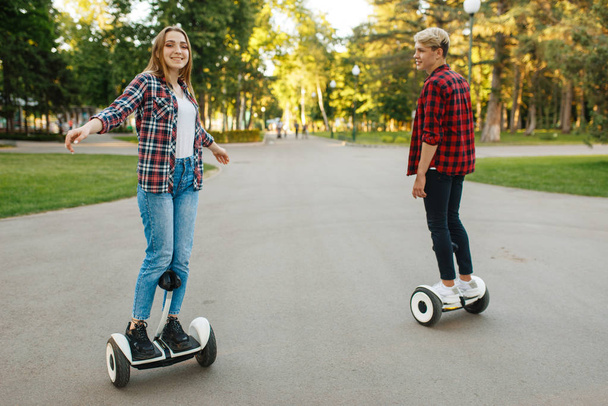 Jeune couple chevauchant sur mini gyroscope dans le parc d'été. Loisirs de plein air avec gyroboard électrique. Transport avec technologie d'équilibre
 - Photo, image