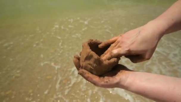 Primo piano di mani che fanno argilla su una spiaggia di mare, sabbia e onda come sfondo, estate e concetto di viaggio
. - Filmati, video