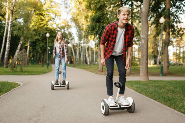 Young couple riding on gyro boards in summer park. Outdoor recreation with electric gyroboard. Eco transport with balance technology, electrical gyroscope vehicle - Photo, Image