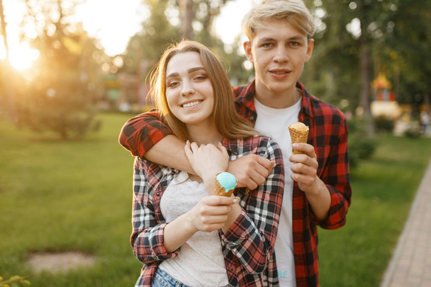 Young love couple with ice cream walking in summer park. Boyfriend and girlfriend leisures with ice-cream, romantic walk - Photo, Image