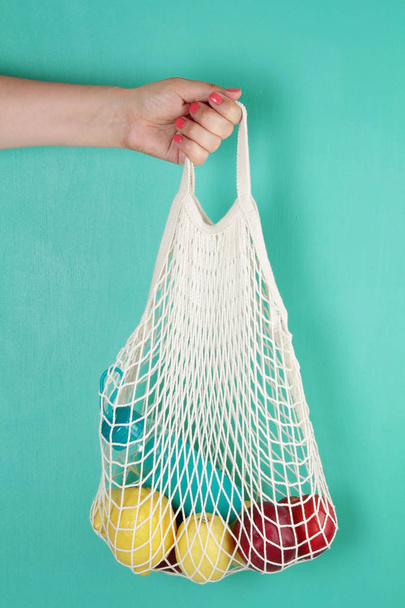 Reusable shopping mesh bag with lemons, fruits and glass bottle. - Foto, Bild