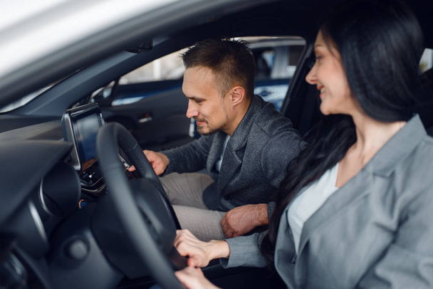 Happy couple buying new car in showroom, woman behind the wheel. Male and female customers choosing vehicle in dealership, automobile sale - Zdjęcie, obraz
