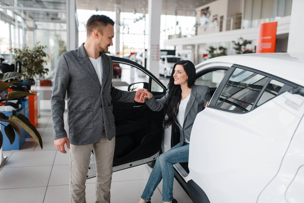 Man and woman buying new car in showroom. Male and female customers choosing vehicle in dealership, automobile sale, auto purchase - Photo, Image