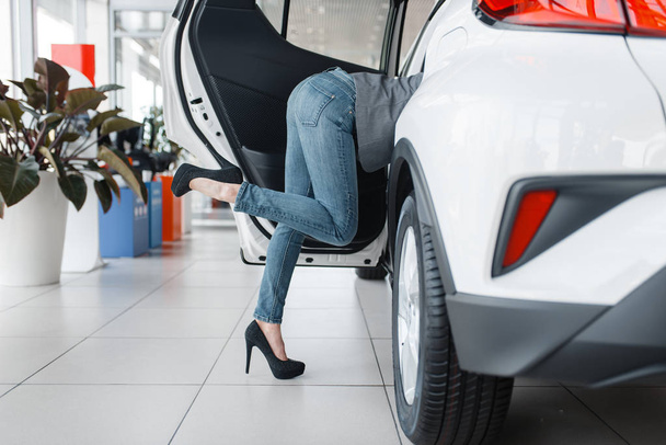 Atrakcyjna kobieta tyłek wystaje z nowego samochodu w Showroom. Kobieta klienci wybierając pojazd w dealerze, sprzedaż samochodów, Auto zakupu - Zdjęcie, obraz