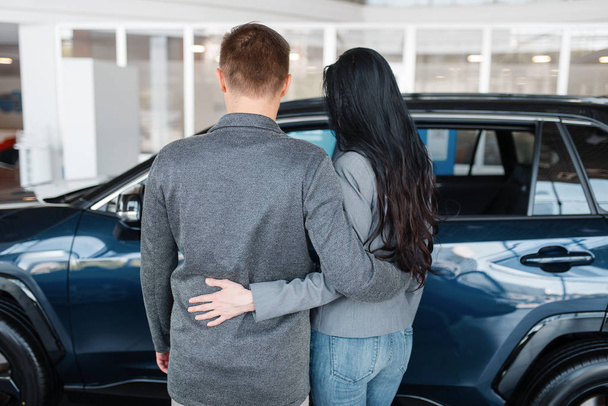 Couple choosing new car in showroom, back view. Male and female customers looks vehicle in dealership, automobile sale, auto purchase - Fotó, kép