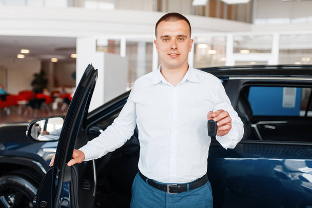 Manager gives key to the new car in showroom. Male customer buying vehicle in dealership, automobile sale, auto purchase - Zdjęcie, obraz