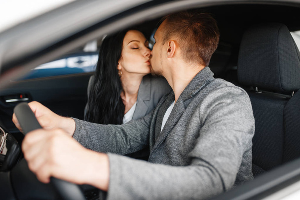 Couple kissing in new car, showroom. Male and female customers buying vehicle in dealership, automobile sale, auto purchase - 写真・画像