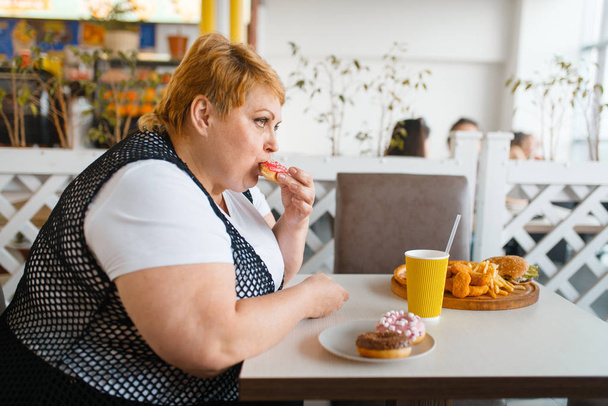 Grosse femme mangeant des beignets dans le restaurant fastfood, des aliments malsains. Femme en surpoids à la table avec un dîner indésirable, problème d'obésité
 - Photo, image
