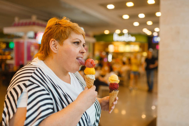 Tlustá žena jedla dvě zmrzliny v restauraci v obchodě s občerstvivím. Nadváha samice s zmrzlinou, problém s obezitou - Fotografie, Obrázek