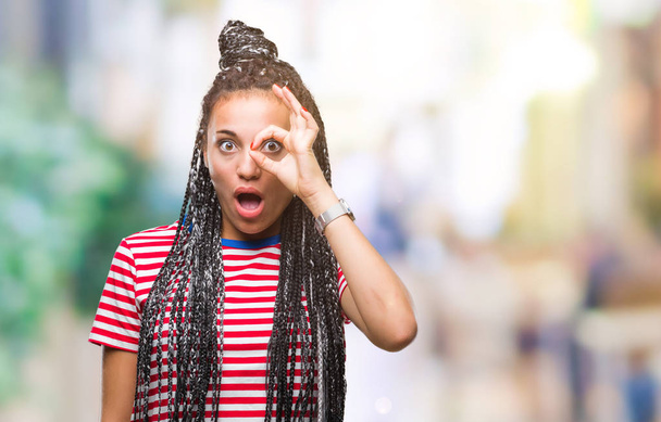 Jeune fille afro-américaine cheveux tressés sur fond isolé faisant geste ok choqué avec visage surpris, oeil regardant à travers les doigts. Expression incrédule
. - Photo, image