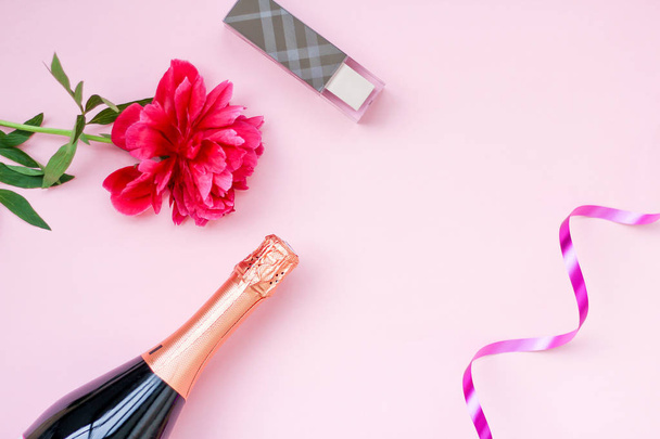 ragazze layout festivo, una bottiglia di champagne, cosmetici, peonia fiore rosso su uno sfondo rosa. posto per testo, vista dall'alto
 - Foto, immagini