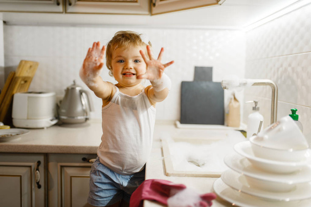 Malá holčička si umyje nádobí v kuchyni. Dítě dělá doma domácí práce. Mladá hospodyňka uklízet dům - Fotografie, Obrázek