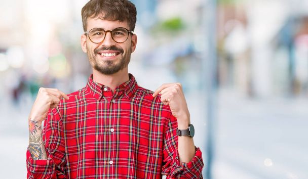 Mladý pohledný muž nosí brýle izolované pozadí sebevědomým úsměvem na tváři, polohovací sebe prsty hrdý a šťastný. - Fotografie, Obrázek