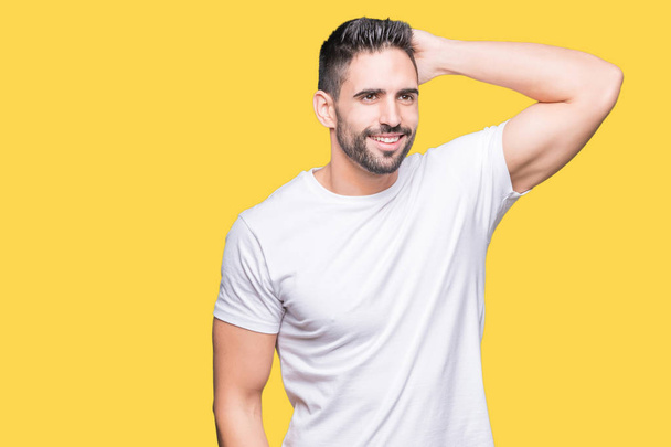 Όμορφος άντρας φορώντας λευκό μπλουζάκι πάνω από κίτρινο απομονωμένο φόντο χαμογελαστός συγκινώντας τα μαλλιά με το χέρι πάνω χειρονομία, θέτοντας ελκυστική - Φωτογραφία, εικόνα