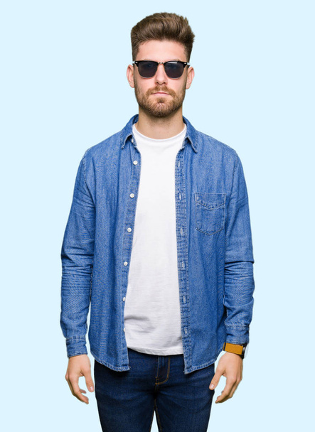 Young handsome elegant man wearing denim jacket with serious expression on face. Simple and natural looking at the camera. - Foto, Imagen