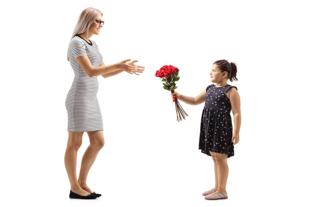 白い背景に孤立した若い女性に赤いバラの束を与える小さな女の子のフルレングスショット - 写真・画像