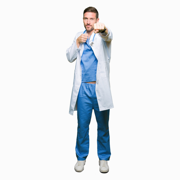 Handsome doctor man wearing medical uniform over isolated background Punching fist to fight, aggressive and angry attack, threat and violence - Foto, afbeelding
