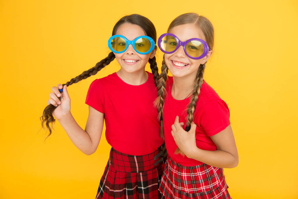 Kids fashionable friends posing in sunglasses on yellow background. Summer fashion trend. Summer fun. Summer accessory. Girls cute sisters similar outfits wear colorful sunglasses for summer season - Zdjęcie, obraz