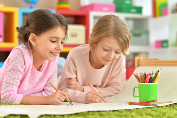 Twee schattige kleine meisjes tekenen met potloden liggend op de vloer - Foto, afbeelding