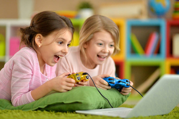 Two pretty little girls lying playing video game  - Foto, imagen