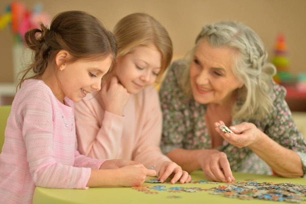 Grandmother with little granddaughters collecting  puzzle - Fotó, kép