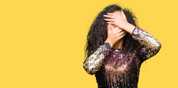 Young beautiful girl with curly hair wearing night party dress Covering eyes and mouth with hands, surprised and shocked. Hiding emotion - Foto, imagen