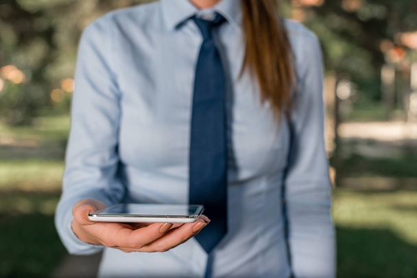 ネクタイをしたシャツを着たビジネスウーマンが、ラップトップの携帯電話を手に持っている。携帯電話・ビジネスウーマンとのコミュニケーションコンセプト. - 写真・画像