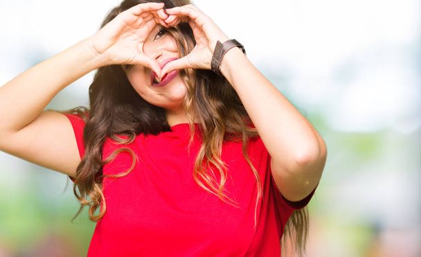 Молода красива жінка в повсякденній футболці робить форму серця з рукою і пальцями посміхаючись дивитися через знак
 - Фото, зображення