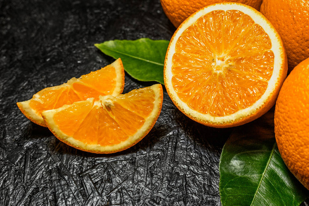 Φέτες και ολόκληρα πορτοκάλια σε σκούρο φόντο - Φωτογραφία, εικόνα