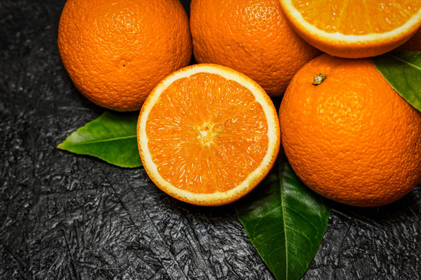 geschnittene und ganze Orangen auf dunklem Hintergrund - Foto, Bild