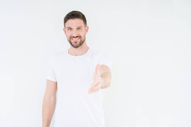 Young handsome man wearing casual white t-shirt over isolated background smiling friendly offering handshake as greeting and welcoming. Successful business. - Foto, Imagem
