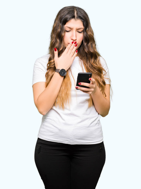 Young adult woman using smartphone cover mouth with hand shocked with shame for mistake, expression of fear, scared in silence, secret concept - Фото, изображение