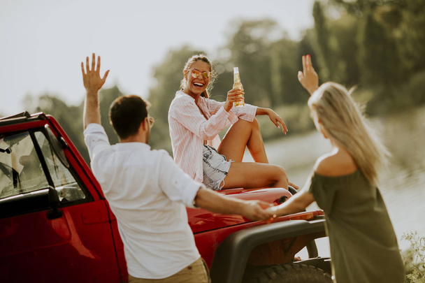 Four young people having fun in convertible car by river - Photo, Image