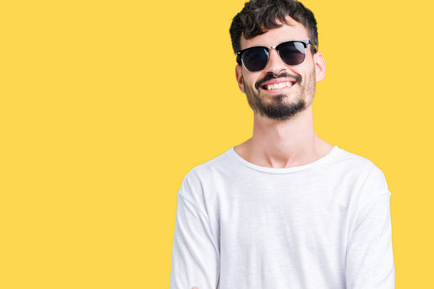 Ein junger gutaussehender Mann mit Sonnenbrille über einem einsamen Hintergrund lächelt glücklich mit verschränkten Armen in die Kamera. positive Person. - Foto, Bild