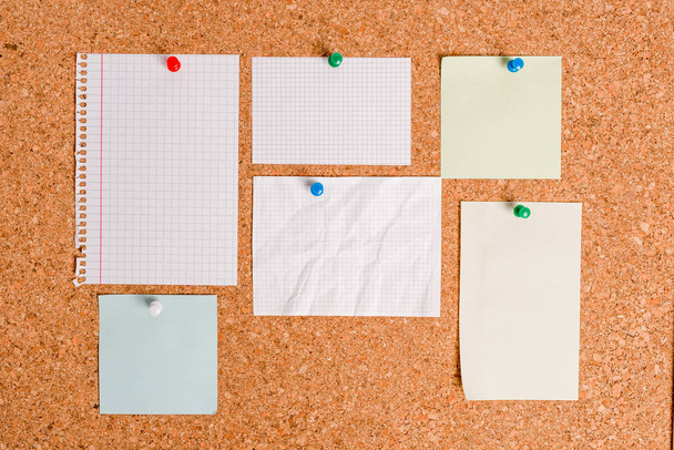 Corkboard with different color and size papers fixed by a pin. Rectangle and square shaped sheets stuck on a billboard by colored thumbtacks. Notice board with empty reminder note. - Photo, Image