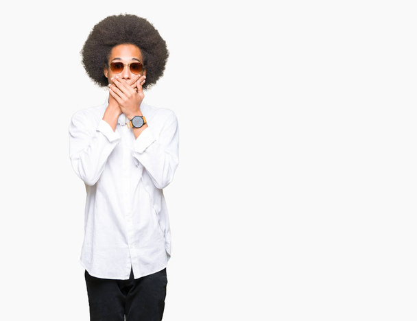 junger afrikanisch-amerikanischer Mann mit Afro-Haaren, Sonnenbrille und Kopfhörer, der fälschlicherweise den Mund mit den Händen bedeckte. Geheimes Konzept. - Foto, Bild
