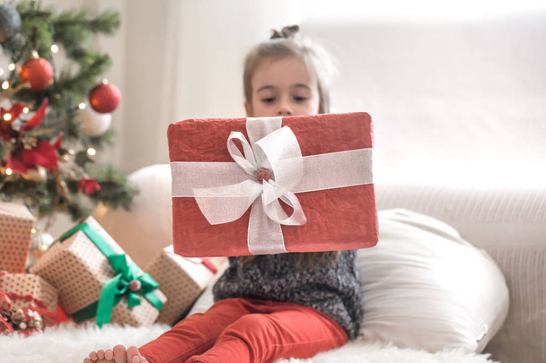 hübsches kleines Mädchen hält eine Geschenkschachtel und lächelt, während sie sitzt - Foto, Bild