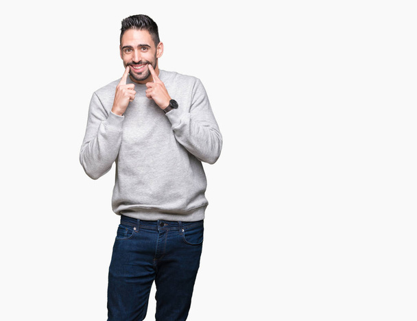 Jonge knappe man dragen sweatshirt over geïsoleerd background Smiling met open mond, vingers wijzen en dwingen vrolijke glimlach - Foto, afbeelding