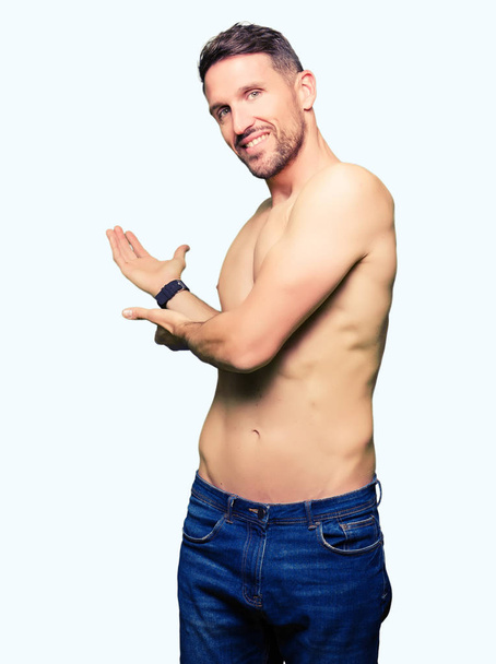 Όμορφος άνδρας shirtless δείχνει γυμνό στήθος προσκαλεί να εισέλθουν χαμογελώντας φυσικά με ανοιχτό χέρι - Φωτογραφία, εικόνα
