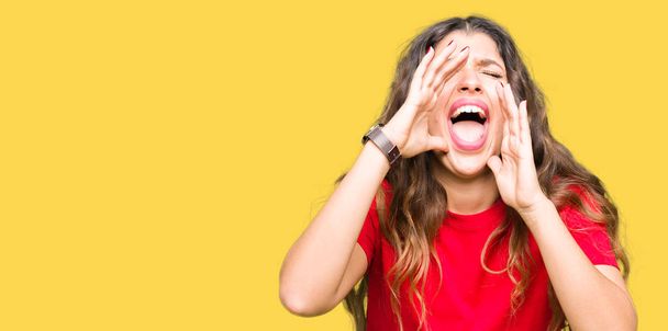 Молодая красивая женщина в повседневной футболке кричит сердито с руками над ртом
 - Фото, изображение