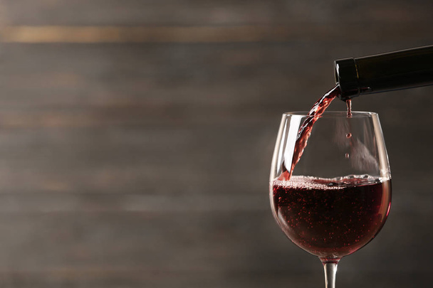 Pouring red wine into glass from bottle against blurred wooden background, closeup. Space for text - Photo, Image